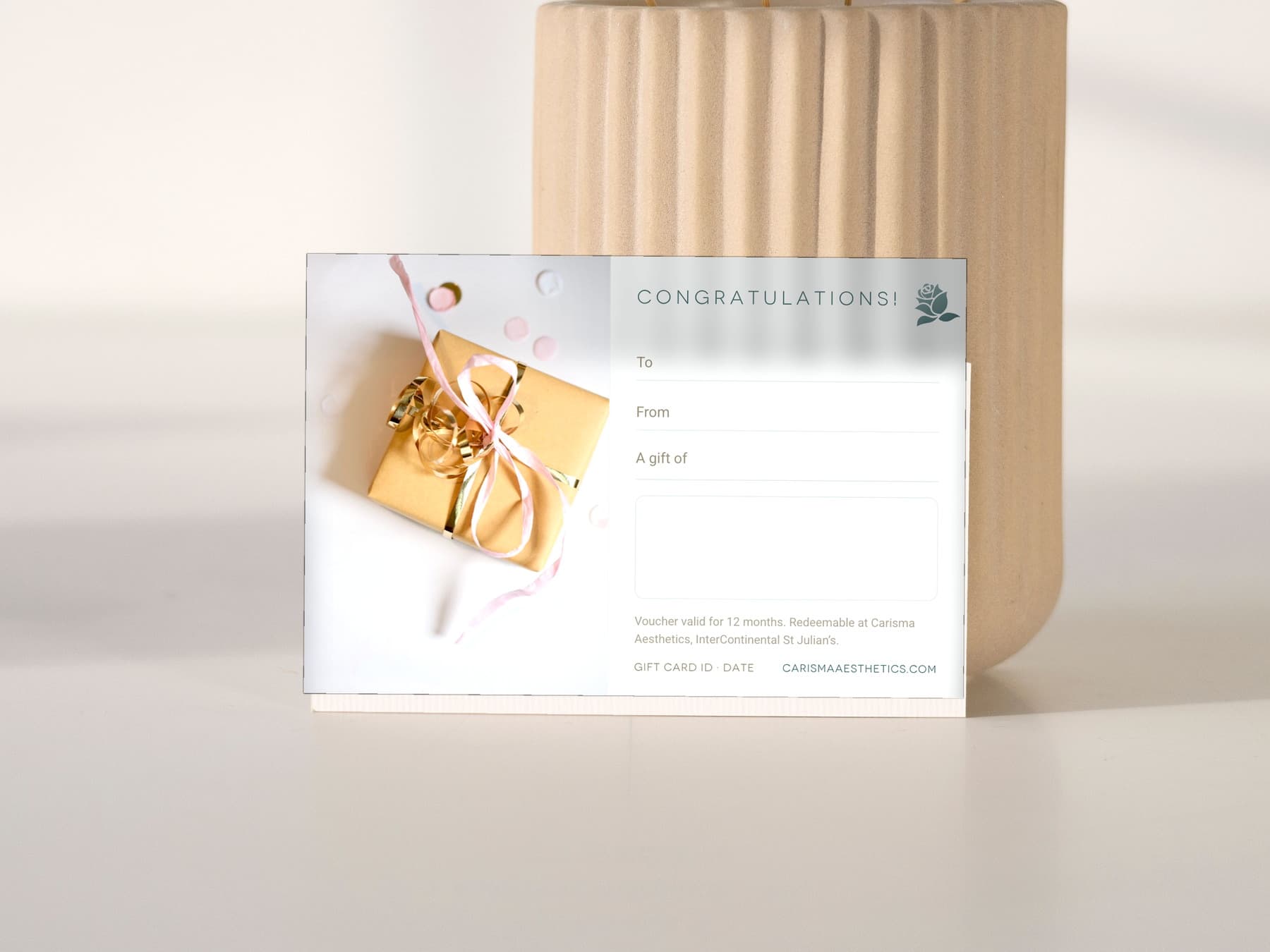 A Carisma Aesthetics congratulations gift card on white linen with an anthurium
