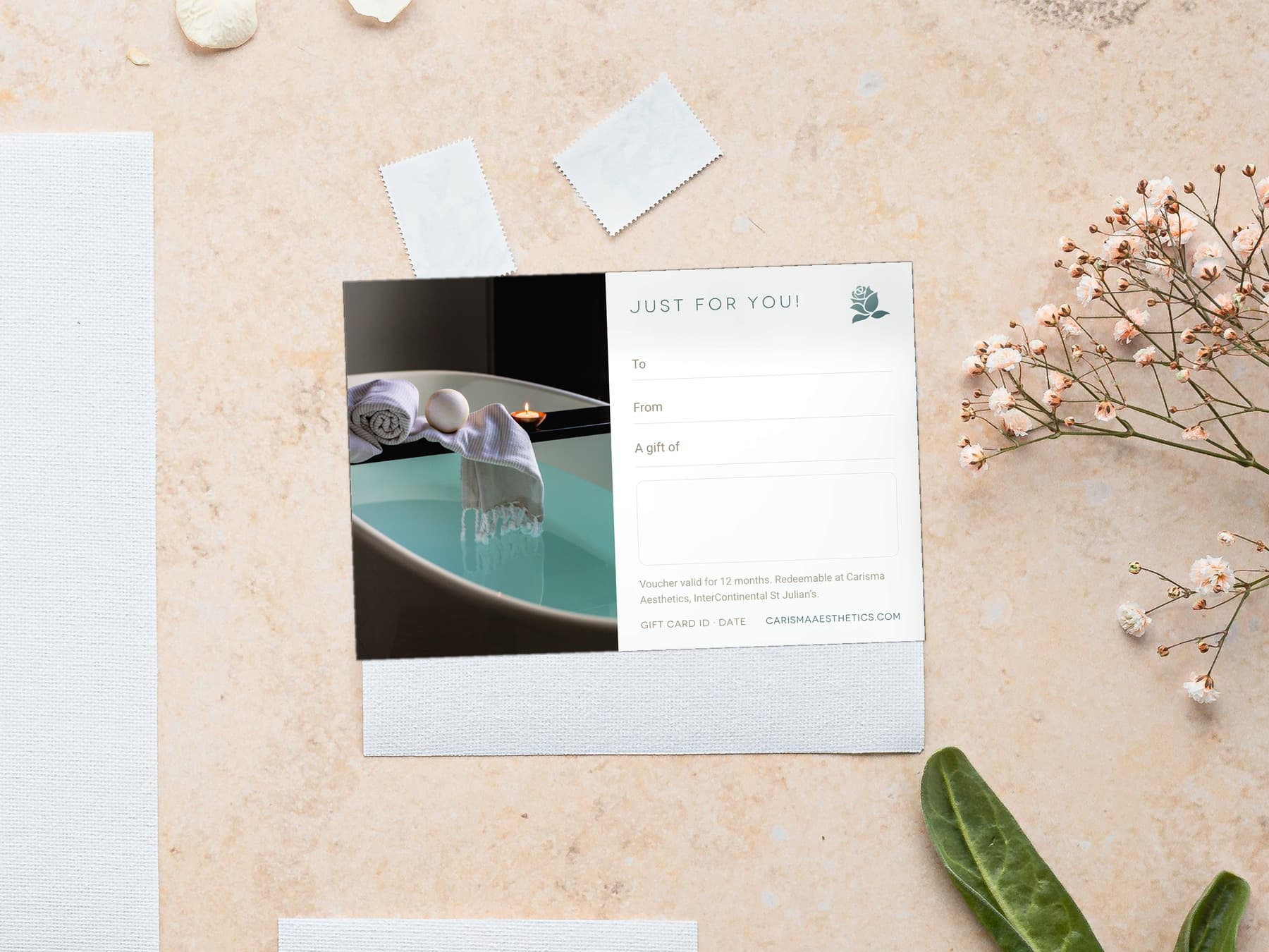 A Carisma Aesthetics gift card on pale plaster with a scallop shell and a white bloom